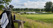 Golftas naast een houten bank met uitzicht op een golfbaan en water.